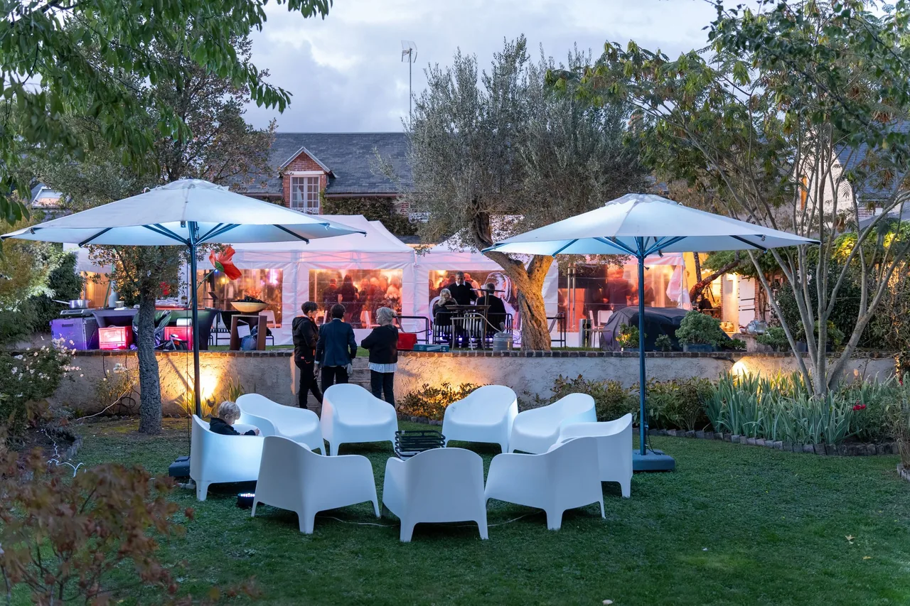 El jardín de la fiesta de los 100 años de Mémé al atardecer: carpas blancas, sombrillas y sillones blancos delante de la casa, en el valle del Loir